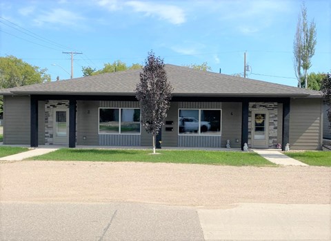 the front of a gray building with a lawn and a tree